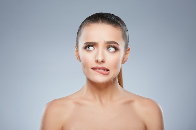 Retrato de belleza de niña tensa mirando a un lado. Cabeza y hombros de hermosa mujer avergonzada mordiéndose los labios nerviosamente. Maquillaje natural, estudio, emociones