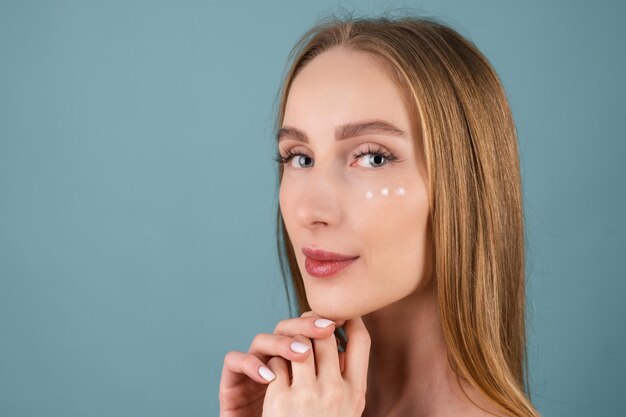 Retrato de belleza de primer plano de una mujer en topless con piel perfecta y maquillaje natural, con puntos de crema antienvejecimiento para hidratar y reafirmar la piel debajo de los ojos