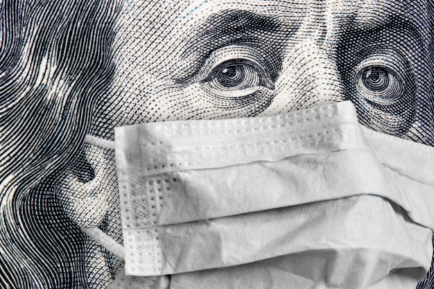 Retrato de Benjamin Franklin cerca de billetes de 100 dólares en una máscara médica