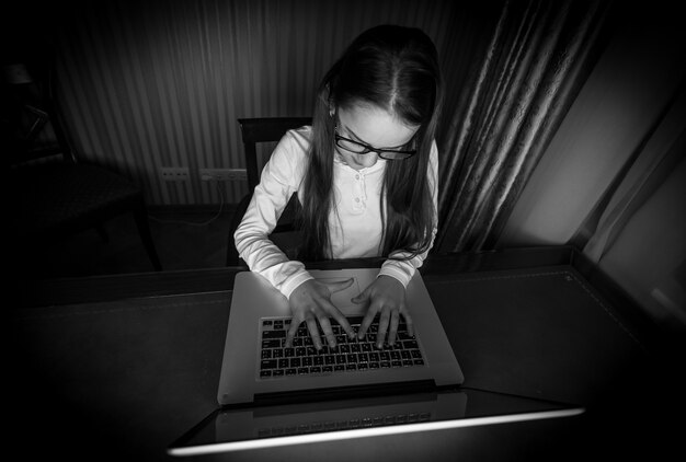 Foto retrato en blanco y negro de una adolescente sentada en una habitación oscura con un portátil