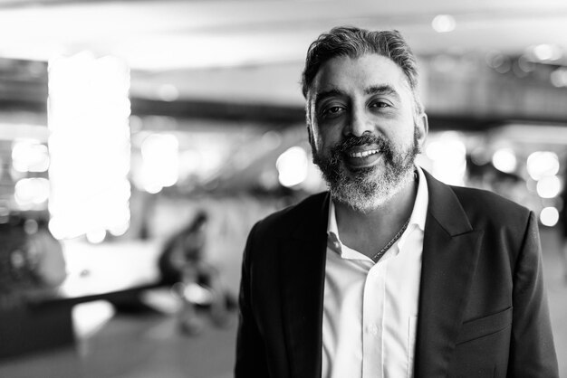 Retrato en blanco y negro del apuesto empresario indio en la ciudad por la noche sonriendo