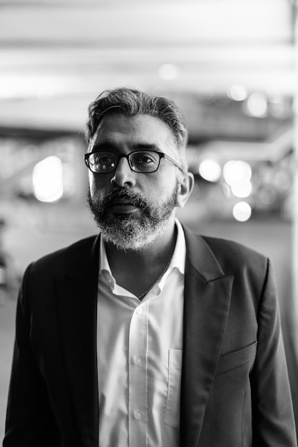 Retrato en blanco y negro del apuesto hombre de negocios indio en la ciudad por la noche pensando