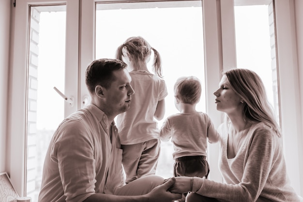 Retrato en blanco y negro de familia caucásica mirando por la ventana