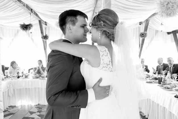 Retrato en blanco y negro de felices recién casados bailando en el restaurante