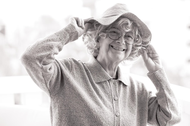 Retrato en blanco y negro de feliz hermosa anciana rizada con sombrero y gafas de sol