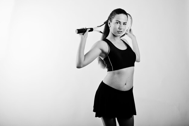 Retrato en blanco y negro de una hermosa joven jugadora con ropa deportiva sosteniendo una raqueta de tenis mientras se enfrenta a un fondo blanco