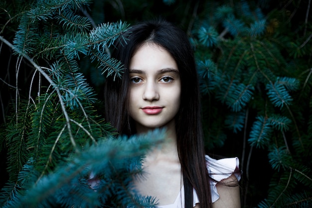 Retrato en blanco y negro de una hermosa jovencita posando entre las ramas de pino.