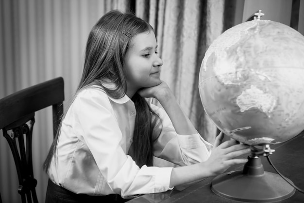 Retrato en blanco y negro de linda colegiala mirando gran globo en la mesa