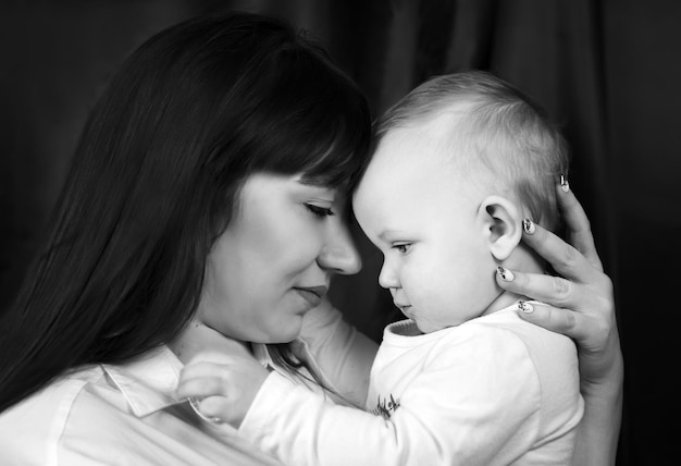 Retrato en blanco y negro de una madre con una hija de un año Mamá sostiene al niño al nivel de su cabeza, se tocan la frente con la cabeza inclinada mirándose el uno al otro