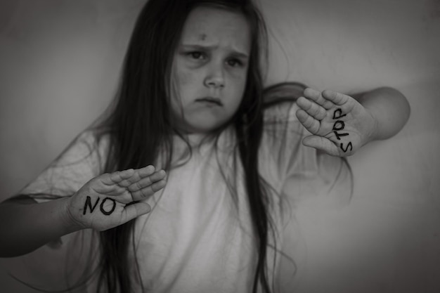 Foto retrato en blanco y negro de una niña asustada y asustada de pie levantando las manos mostrando la inscripción sin parar en las palmas