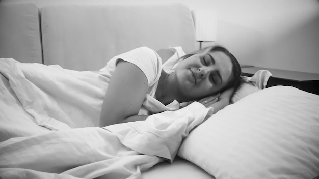 Retrato en blanco y negro de sonriente joven durmiendo en la cama por la noche.