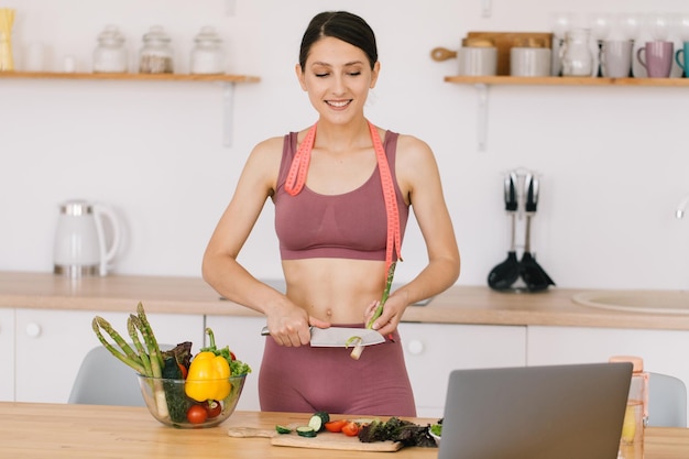 Retrato de una bloguera deportiva feliz haciendo espárragos cocinando y dirigiendo una videoconferencia sobre el tema de la alimentación saludable en una laptop en la cocina