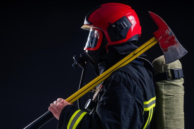 Foto retrato bombeiro forte em uniforme à prova de fogo segurando um machado nas mãos estúdio de fundo preto