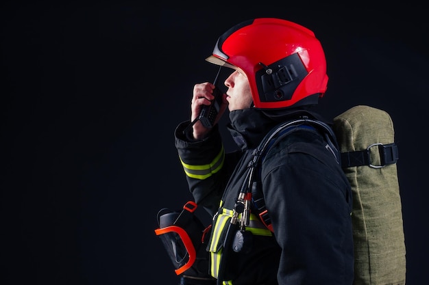 Retrato bombero fuerte en uniforme ignífugo sosteniendo un hacha en sus manos estudio de fondo negro