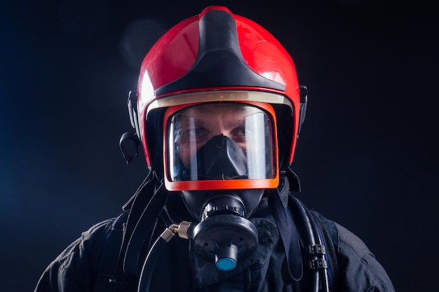 Retrato bombero fuerte en uniforme ignífugo sosteniendo una motosierra hacha en sus manos estudio de fondo negro.máscara de oxígeno en la cabeza de cerca