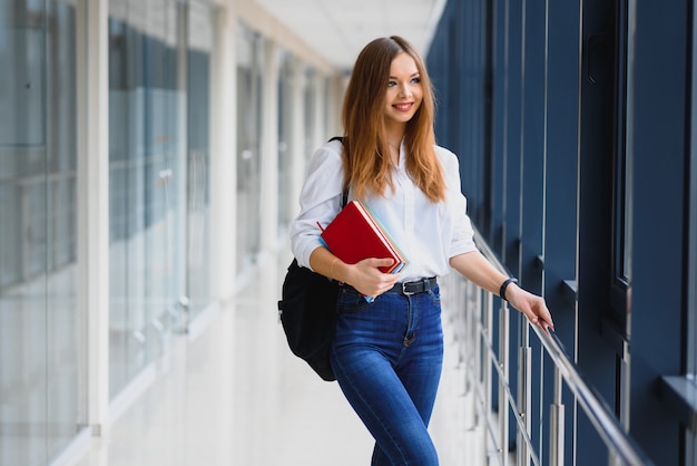 Retrato de una bonita estudiante con libros y una mochila en el pasillo de la universidad