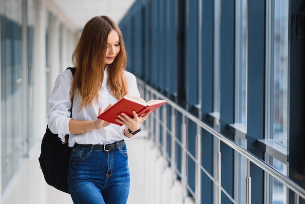 Retrato de una bonita estudiante con libros y una mochila en el pasillo de la universidad