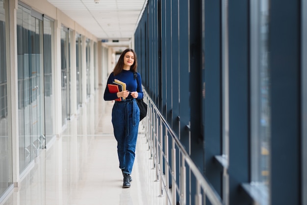 Retrato de una bonita estudiante con libros y una mochila en el pasillo de la universidad