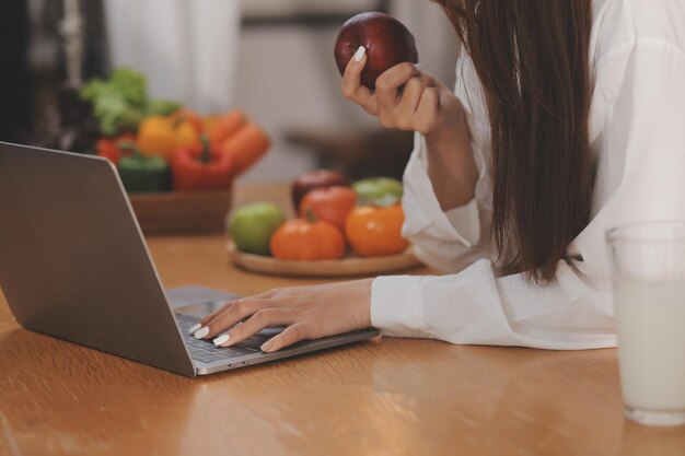 Retrato de una bonita mujer independiente que trabaja escribiendo en una computadora portátil sentada en la mesa sonriendo mirando la pantalla en la cocina Una atractiva mujer joven pelirroja que trabaja remotamente en una laptop desde la oficina de casa