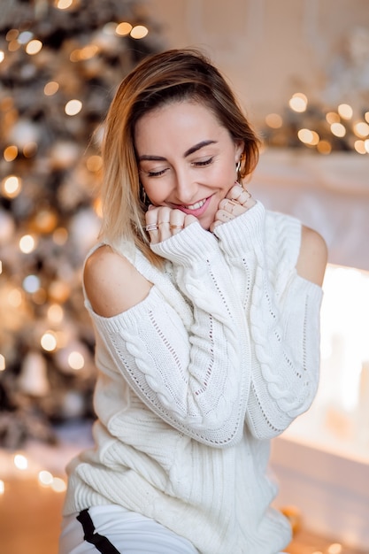 Retrato de una bonita rubia con un acogedor suéter de casa en el árbol de Navidad