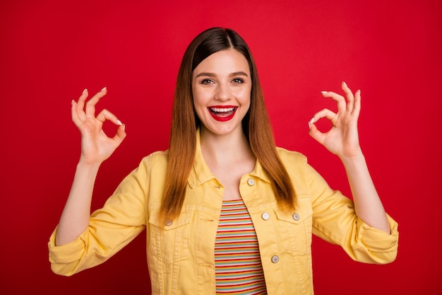 Retrato de bonito atractivo encantador bastante encantador contenido alegre alegre chica pelirroja que muestra dos anuncios publicitarios de doble signo ok aislado sobre fondo de color rojo vibrante de brillo vivo brillante