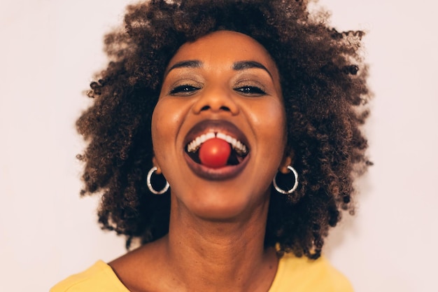 Retrato bonito de mulher afro-americana com tomate cereja nos dentes foco nos olhos