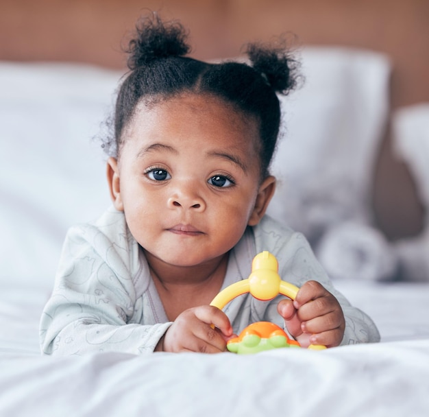 Retrato bonito e bebê com um brinquedo em sua cama brincando e relaxando em seu berçário moderno infância lúdica e menina africana bebê ou recém-nascido brincando com objeto de plástico em seu quarto em sua casa