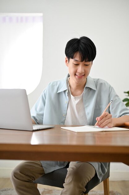 Retrato Bonito jovem estudante universitário asiático fazendo lição de casa tomando notas