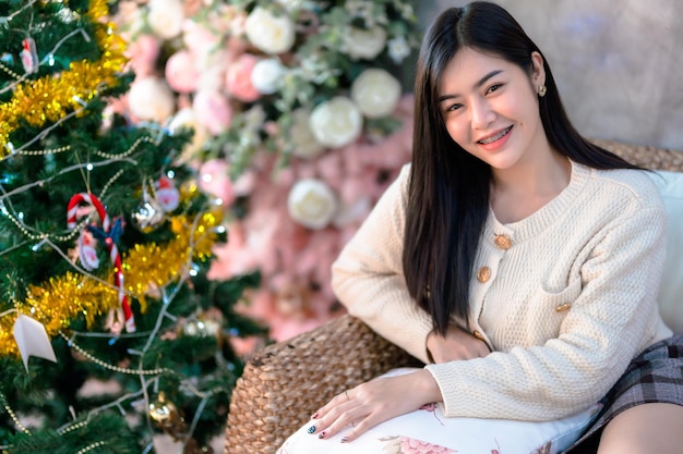 Retrato Bonito lindo sorriso positivo jovem mulher asiática decorando uma árvore de Natal em casa na sala de estar Decoração durante o Natal Natal e feriados de Ano Novo