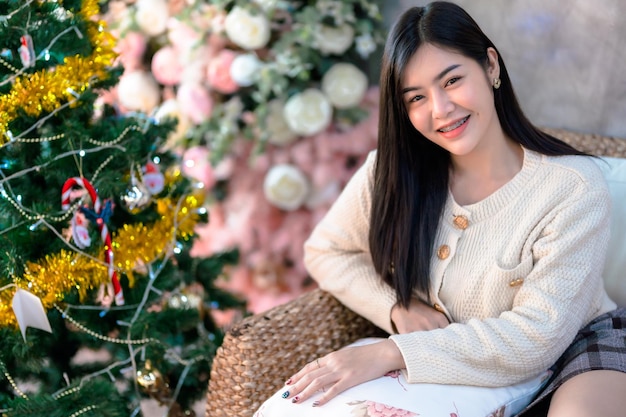 Retrato bonito lindo sorriso positivo jovem mulher asiática decorando uma árvore de natal em casa na sala de estar decoração durante o natal natal e feriados de ano novo