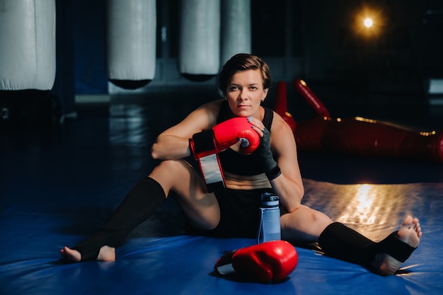 Retrato de una boxeadora en guantes rojos en el gimnasio después del entrenamiento