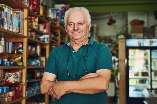 Retrato de brazos cruzados y hombre sénior en la tienda para administrar una tienda minorista inicial como empresario Propietario de una tienda y un pequeño negocio con persona feliz en el taller para inspeccionar el inventario o las existencias