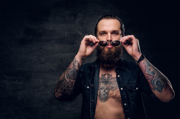 Retrato de un brutal hombre barbudo con tatuajes en un estudio fotográfico oscuro.