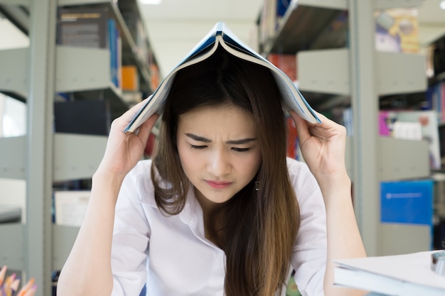 Retrato de la cabeza de la cubierta del estudiante con el libro mientras que lee el libro en biblioteca de la universidad. Concepto de educación.