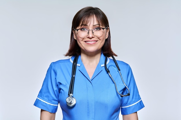 Retrato en la cabeza de una enfermera con uniforme azul mirando a la cámara con un fondo claro de estudio