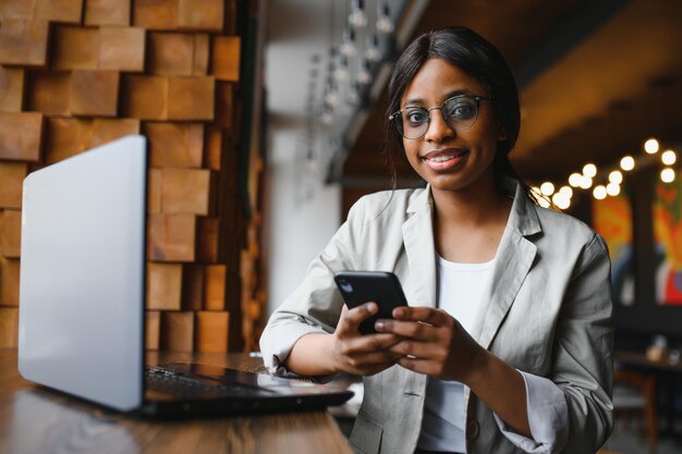 Retrato en la cabeza de una feliz y sonriente mujer afroamericana sentada en la mesa de un café mirando a la cámara emocionada mujer posando trabajando en la computadora haciendo la tarea preparando un informe en la cafetería