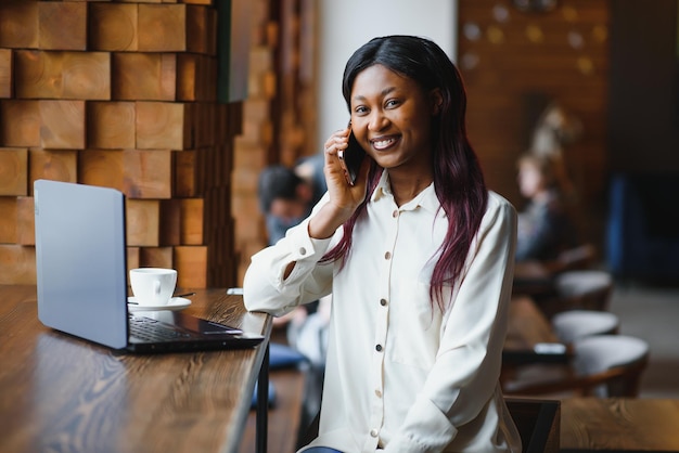 Retrato en la cabeza de una feliz y sonriente mujer afroamericana sentada en la mesa de un café mirando a la cámara emocionada mujer posando trabajando en la computadora haciendo la tarea preparando un informe en la cafetería