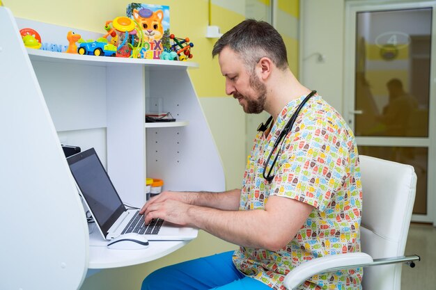 Retrato en la cabeza de un joven médico sonriente con uniforme médico brillante Sentado en el escritorio y escribiendo en el cuaderno El médico muestra habilidades de confianza en el lugar de trabajo de la clínica