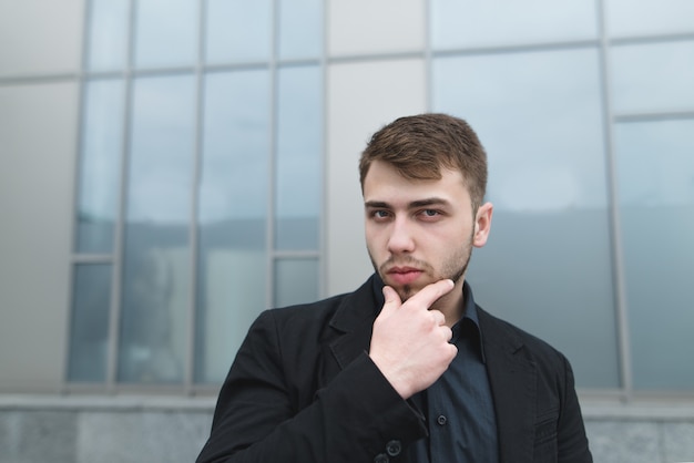 Retrato de la calle de un apuesto joven empresario posando en la pared gris.