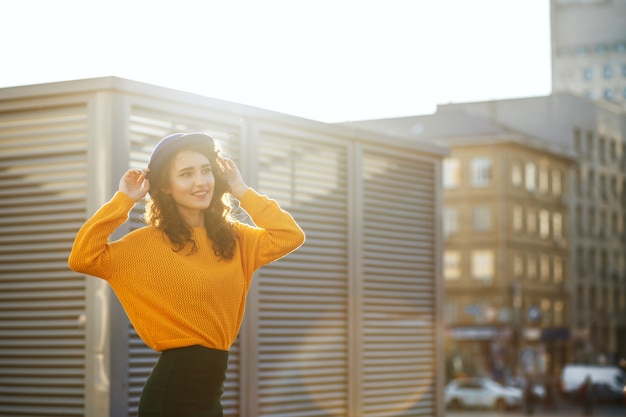 Foto retrato de la calle de la hermosa niña con sombrero azul y suéter de punto amarillo posando en los rayos del sol. espacio para texto