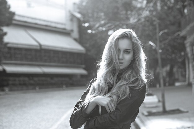 Retrato de la calle de modelo rubia seductora con pelo rizado y exuberante lleva abrigo. Mujer camina en un día soleado en la calle de Kiev. Espacio vacio. Tono monocromo