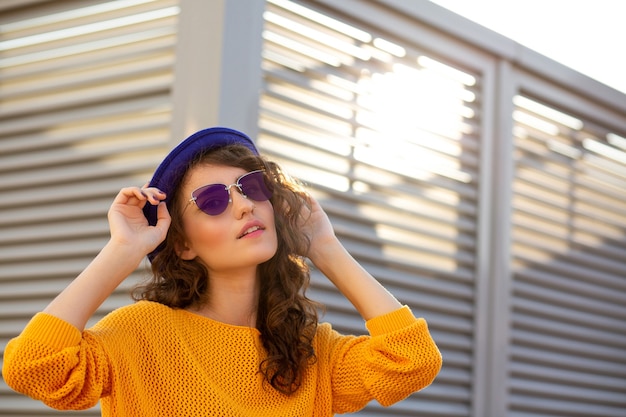 Retrato de la calle de mujer glamour con sombrero azul y gafas posando con resplandor del sol. Espacio para texto