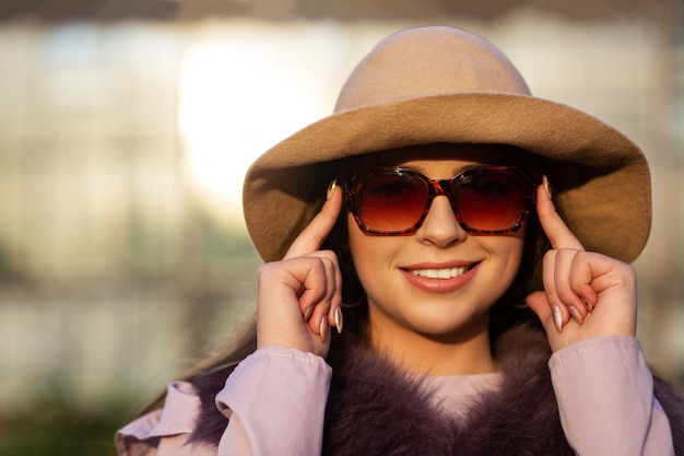 Retrato de calle de mujer morena positiva lleva sombrero y gafas de sol, disfrutando de un clima cálido. Espacio para texto