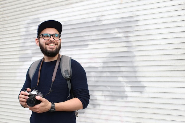 Retrato callejero de un fotógrafo masculino con barba en gafas y una gorra con una cámara de fotos vintage