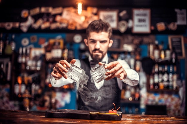 Retrato de camarero agrega ingredientes a un cóctel mientras está de pie cerca de la barra del bar en el pub