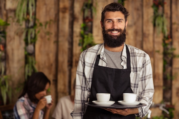 Foto retrato de camarero sosteniendo una taza de café en la bandeja de servir