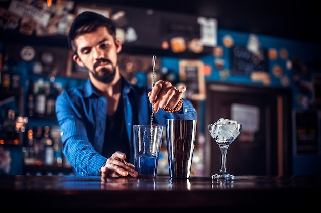 Retrato de camarero vertiendo bebida alcohólica fresca en los vasos mientras está de pie cerca de la barra del bar en el bar