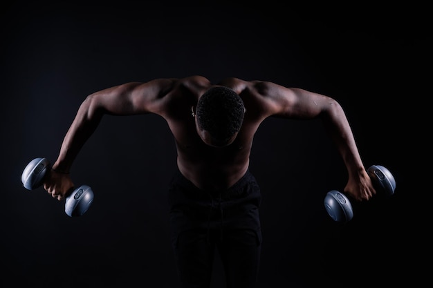 Retrato sin camisa de un joven confiado entrenando con pesas contra fondo negro