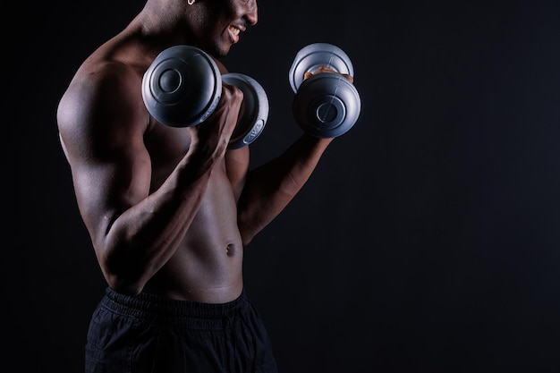 Retrato sin camisa de un joven confiado entrenando con pesas contra fondo negro