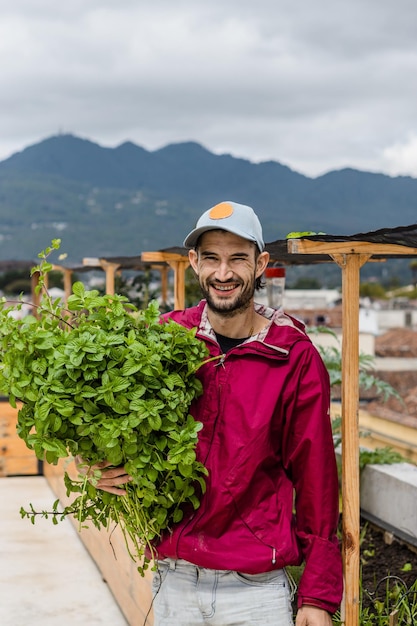 Retrato de un campesino con plantas de menta en las manos sonriendo y mirando a la cámara.